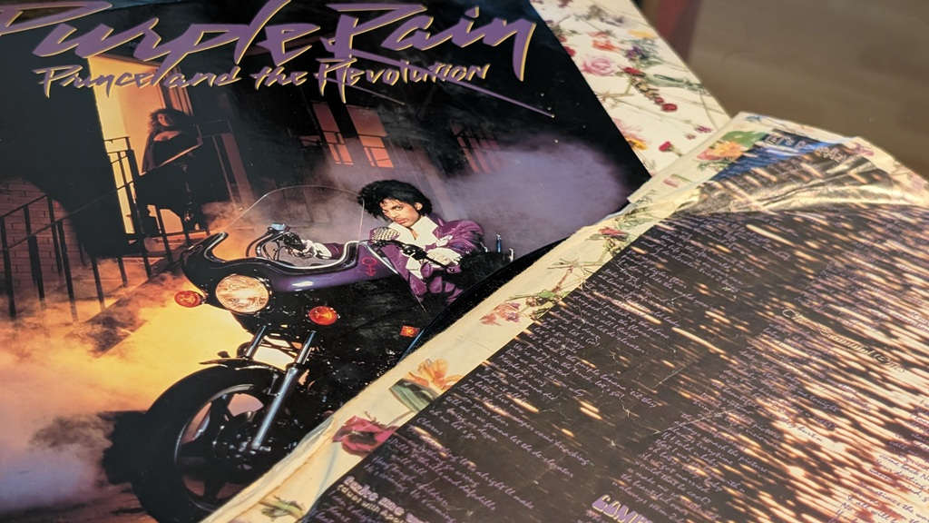 LP von „Purple Rain“ von Prince and the Revolution mit Albumcover und geöffneter Innenhülle auf einer gemusterten Oberfläche.